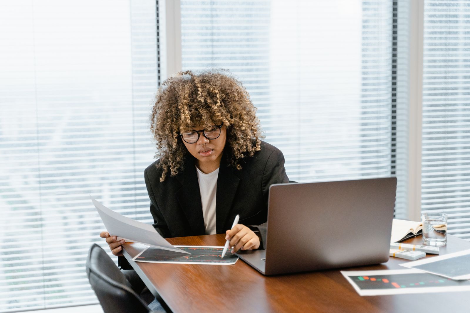 A woman at a desk comparing a printed chart with her notes, with a laptop open beside her