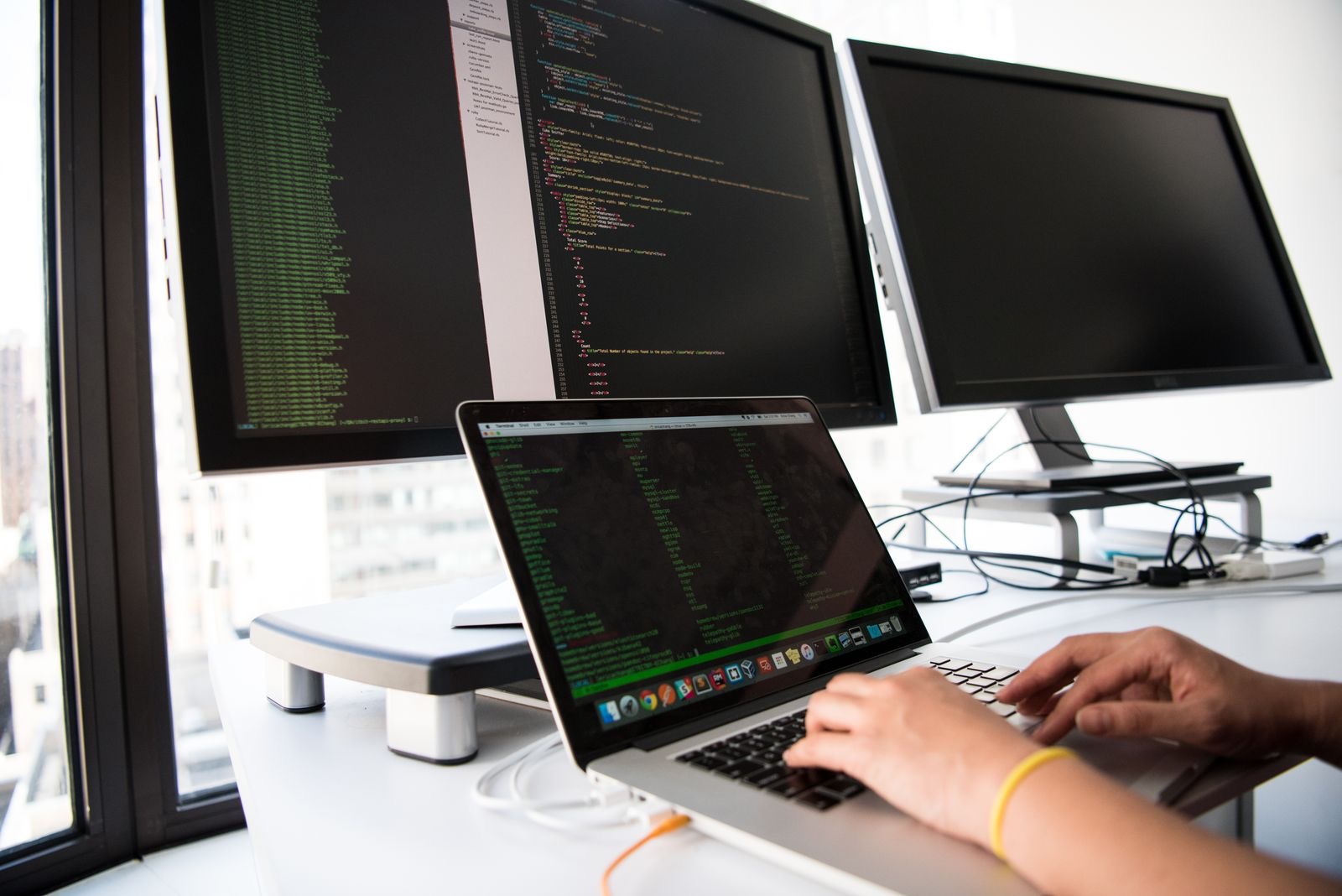 A person writing code on a laptop, with monitors behind them, the kind of Python work a UK data analyst actually does