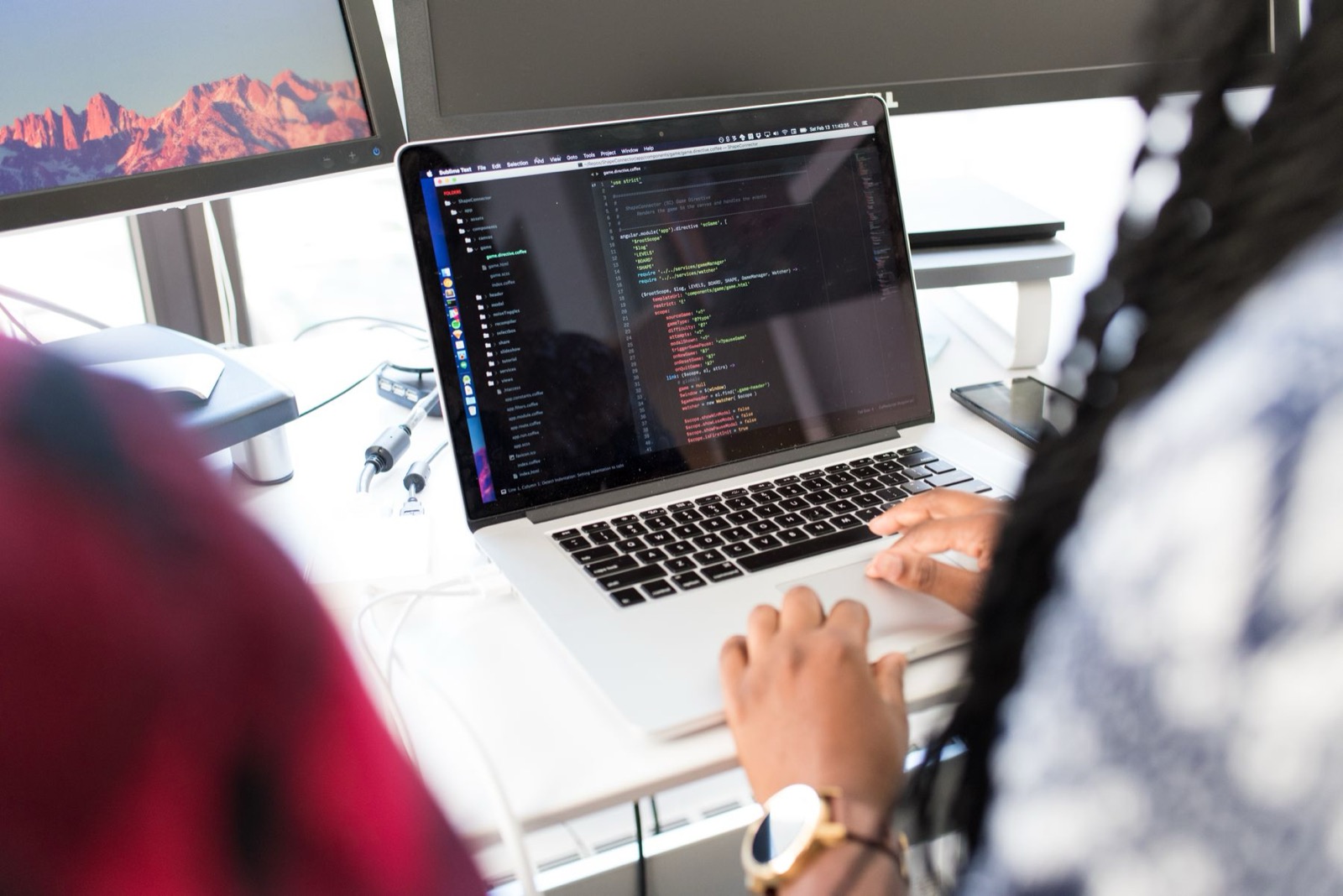 A person writing code on a laptop, with a second monitor behind them, the kind of Python work a UK data engineer actually does