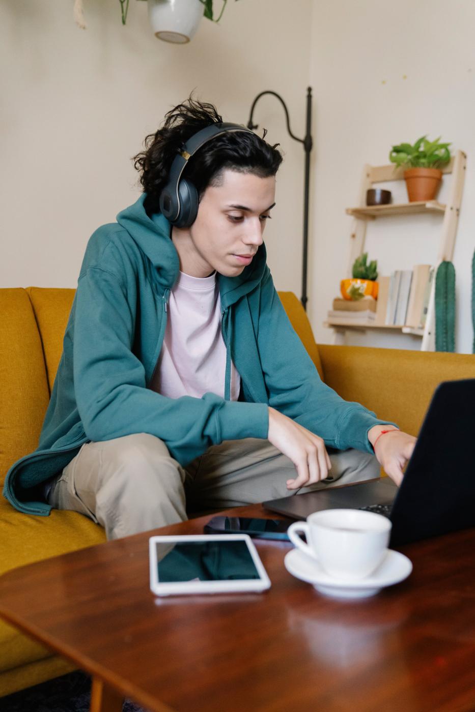 A young man with headphones studying on his sofa