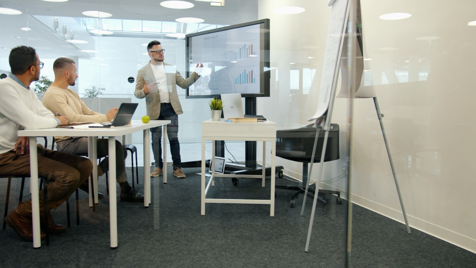 A colleague presenting charts on a screen to two coworkers